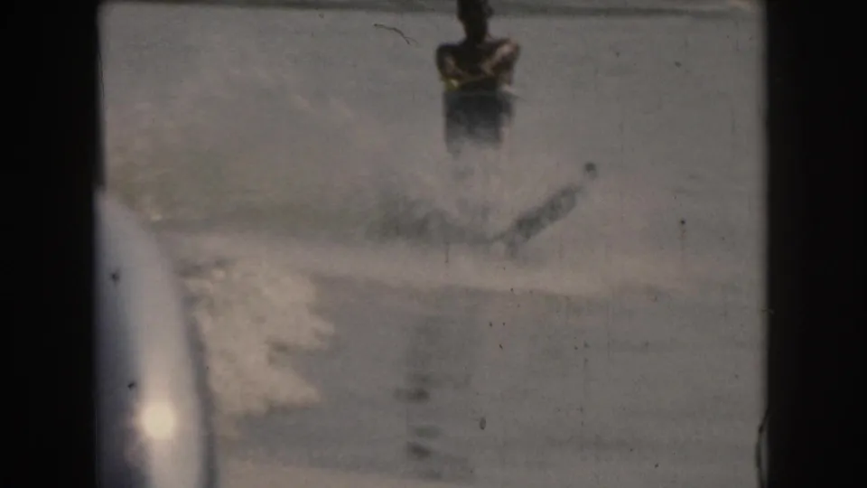 1961 Grand Rapids 8mm frame with a man on water skis moving through spray beside the boat wake on smooth water.