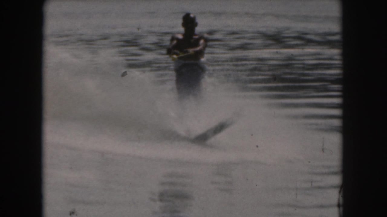 Water skier approaches across a calm lake, with spray beginning behind the skis.