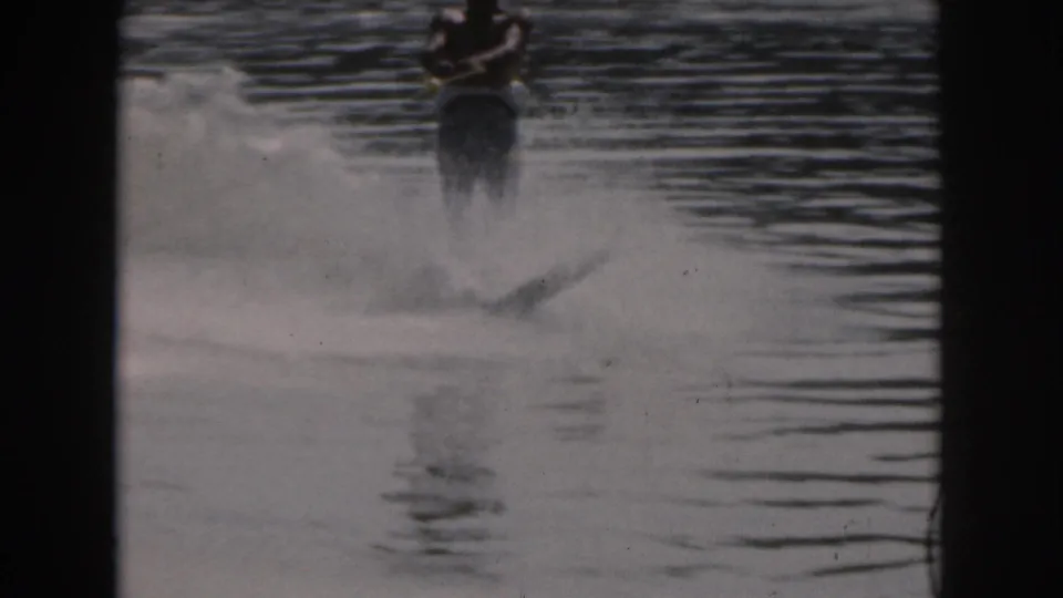 A man water skis on a Michigan lake in 1961, with soft 8mm grain and dark frame edges visible.