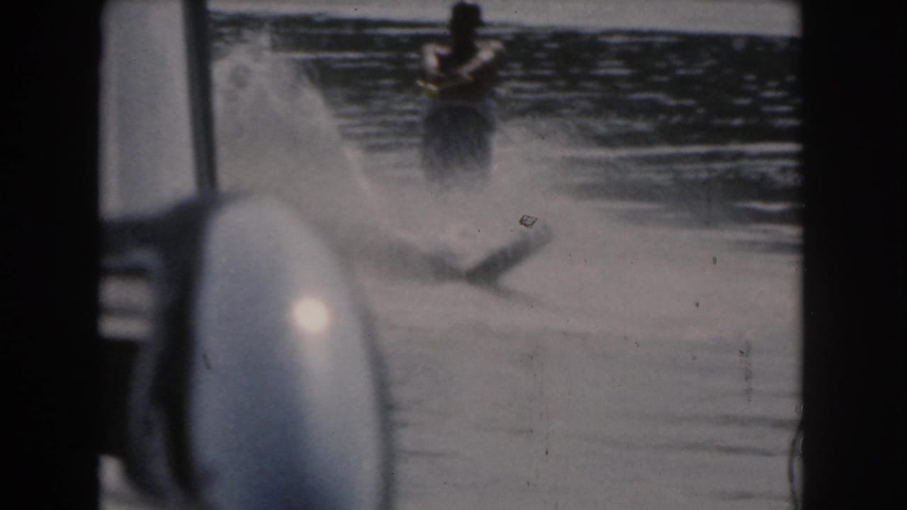 Water skier partly obscured by spray on a lake, seen from inside a boat.