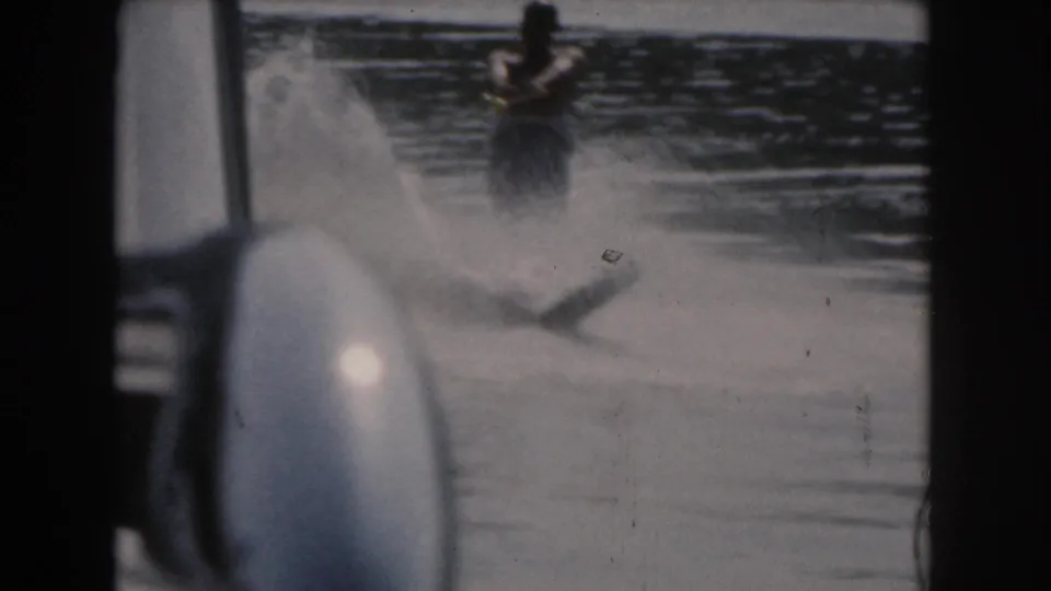 1961 home-movie view near Grand Rapids, Michigan, showing a water skier in spray as the boat interior edges frame the lake.