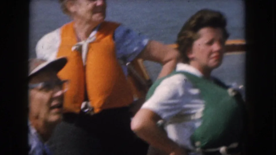Adults wearing bright orange and green life jackets appear close to the camera during the 1961 lake outing near Grand Rapids, Michigan.