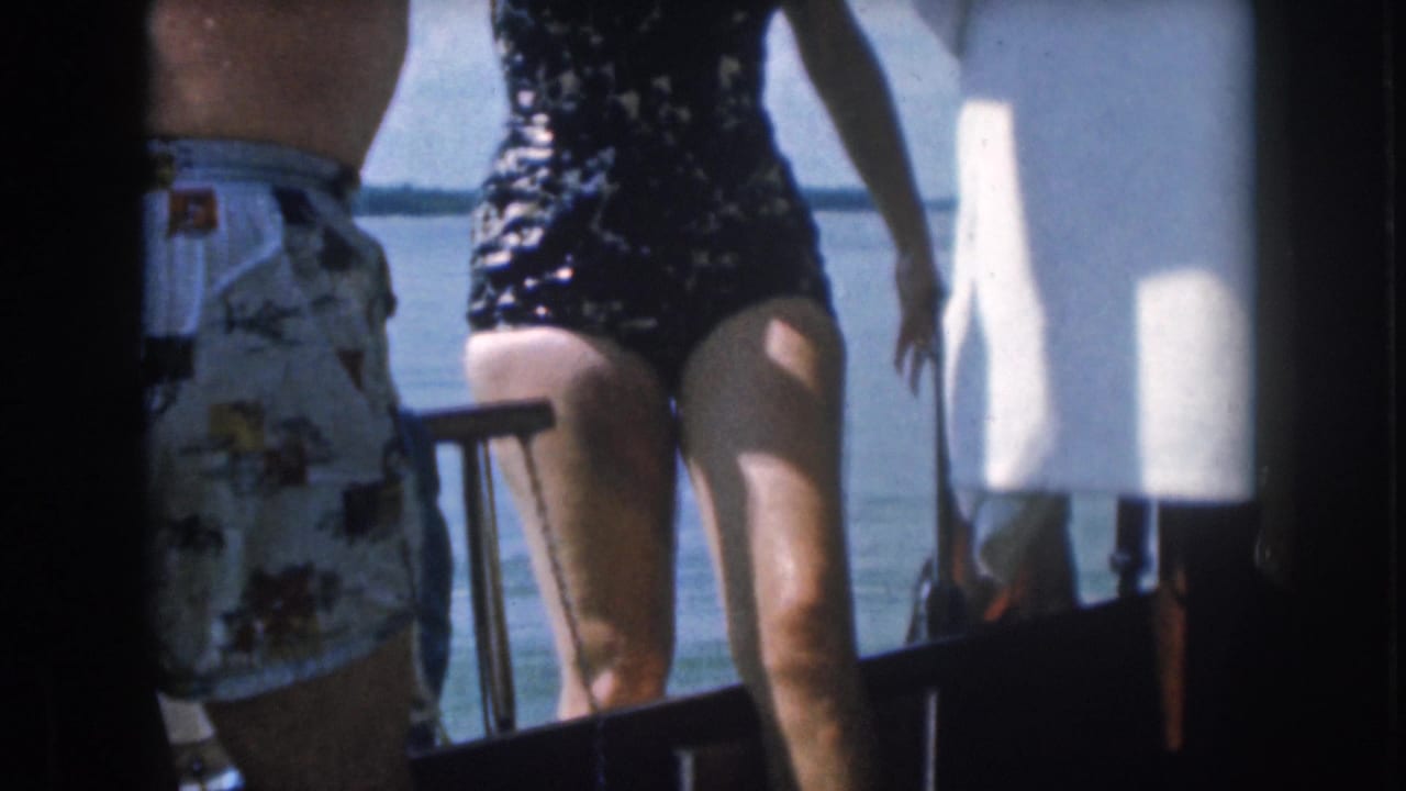 A woman in a dark one-piece swimsuit steps aboard a boat in 1961 Michigan footage, with water and boat hardware behind her.