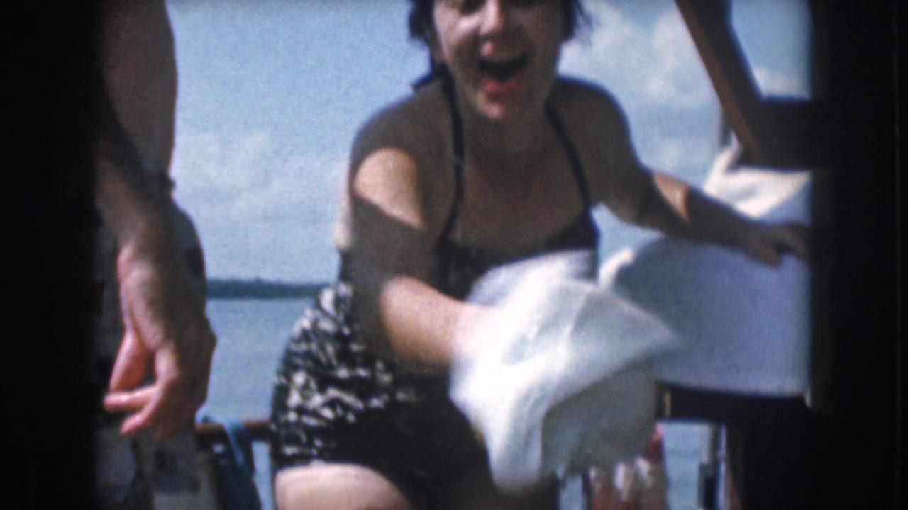 Laughing woman in a dark swimsuit gestures with a white towel on a boat.