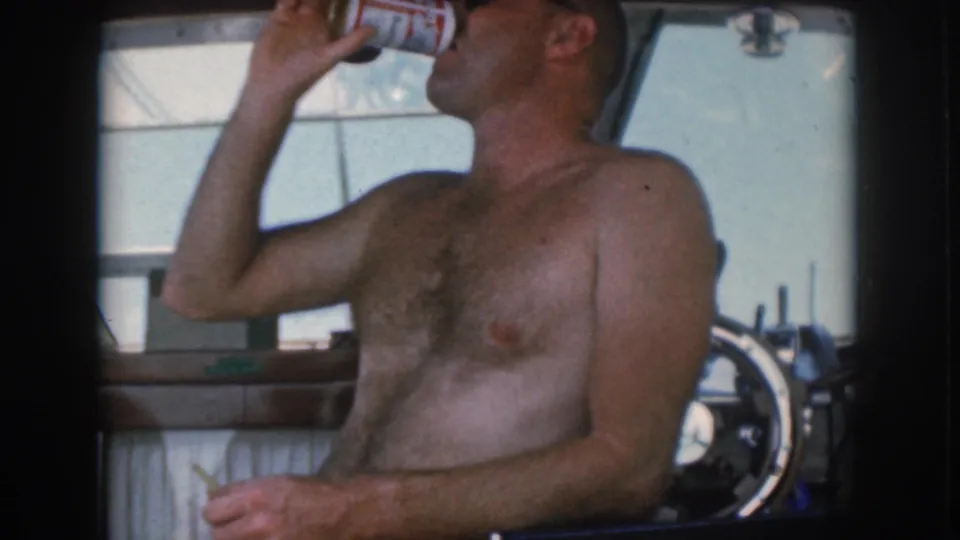 1961 Michigan boating frame showing a shirtless man in sunglasses drinking from a can while seated at the helm.