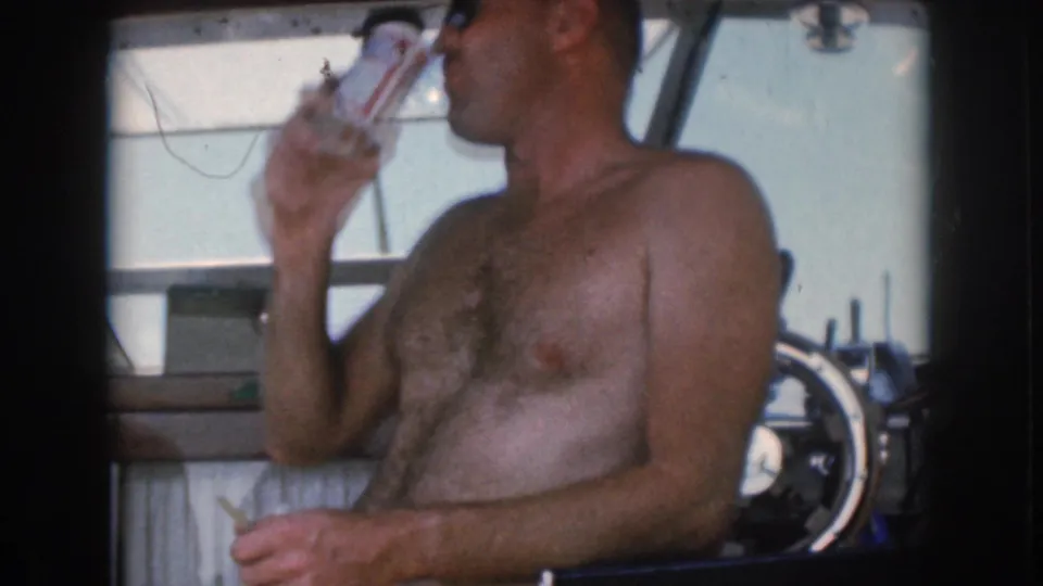 In 1961 home-movie footage from Grand Rapids, Michigan, a shirtless man sits near a motorboat helm and drinks from a can.