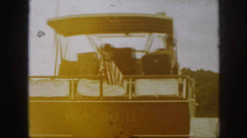 A faded 8mm rear view shows the covered motorboat continuing across a Michigan lake, with seated passengers and the stern flag visible.