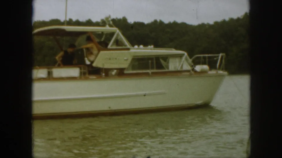 1961 Michigan home-movie frame showing the cruiser passing across the frame, with cabin windows, railings, people, and shoreline visible.