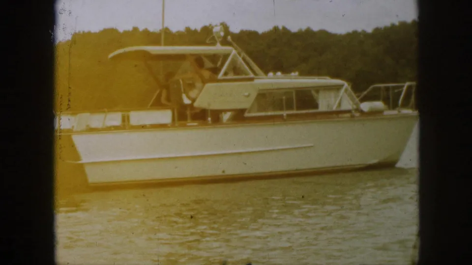 Warm-toned 8mm frame of the 1961 Michigan cabin cruiser passing close to camera on calm water.