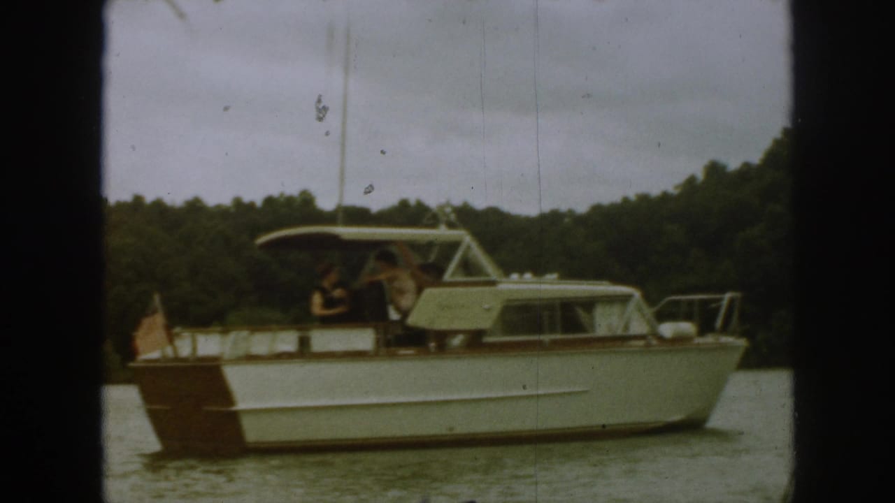 White motorboat with a brown stern passes on a lake beneath a cloudy sky.
