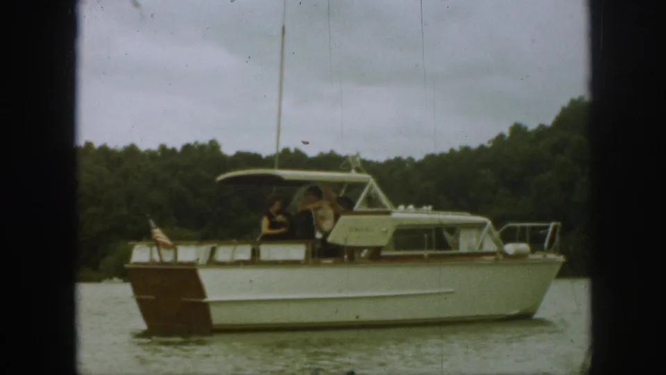 Final 1961 Michigan frame showing the white motorboat moving slowly along the lake, with two people aboard and an American flag at the stern.