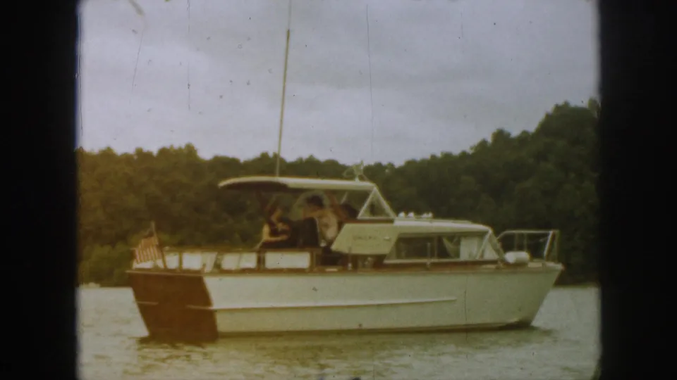 The motorboat remains in side profile on a Michigan lake, with a small U.S. flag at the stern and people visible beneath the canopy.