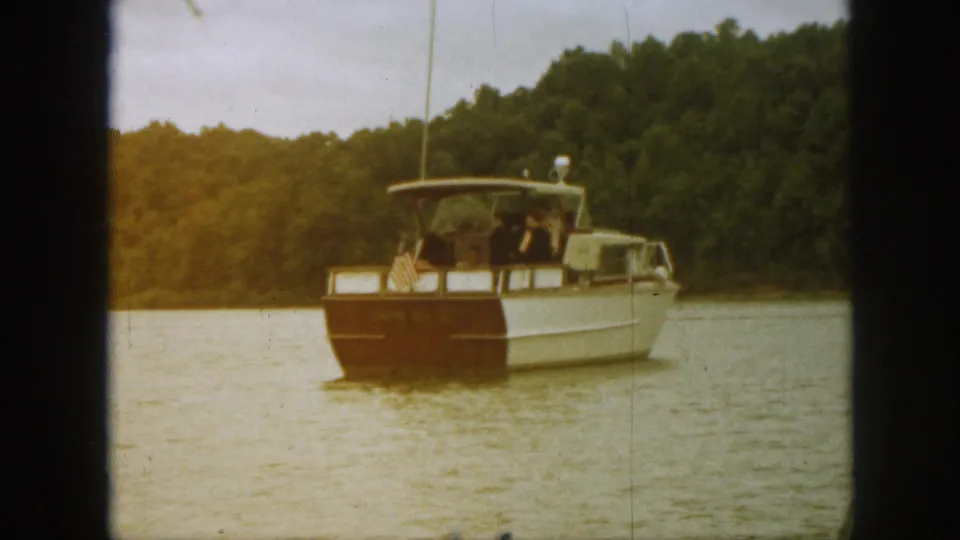 1961 Michigan home-movie frame showing a white and wood tour boat with passengers and a small American flag on a calm lake.