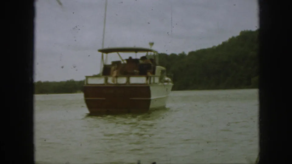 Soft 8mm frame of a tour boat receding on a Michigan lake, with passengers visible under the roof canopy.