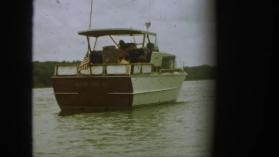 1961 Michigan 8mm frame showing a family-style motorboat on calm lake water with passengers and a small stern flag.