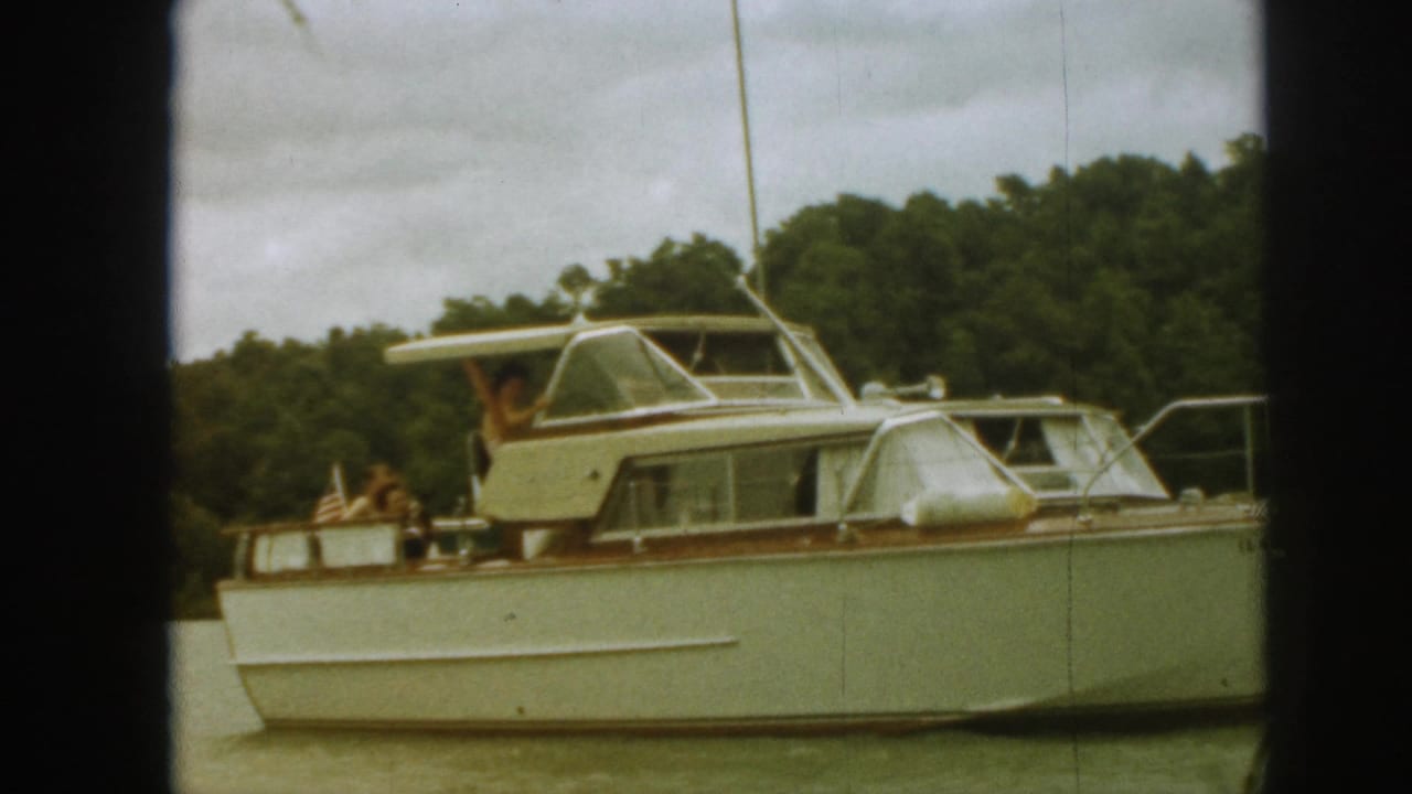 Motor yacht seen from the side with a person waving near the cabin.