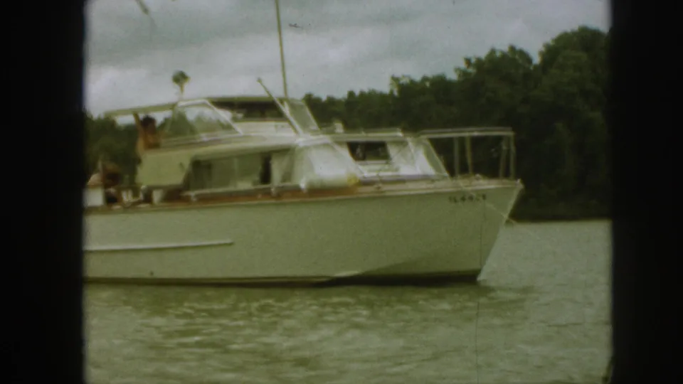 1961 Michigan home-movie frame focusing on the bow and cabin of a white motor yacht, with people partly visible on deck.