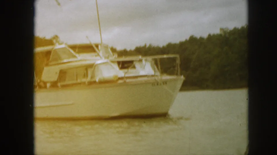 White motor yacht seen through dark 8mm frame borders, with the bow and cabin visible against a wooded Michigan shoreline.