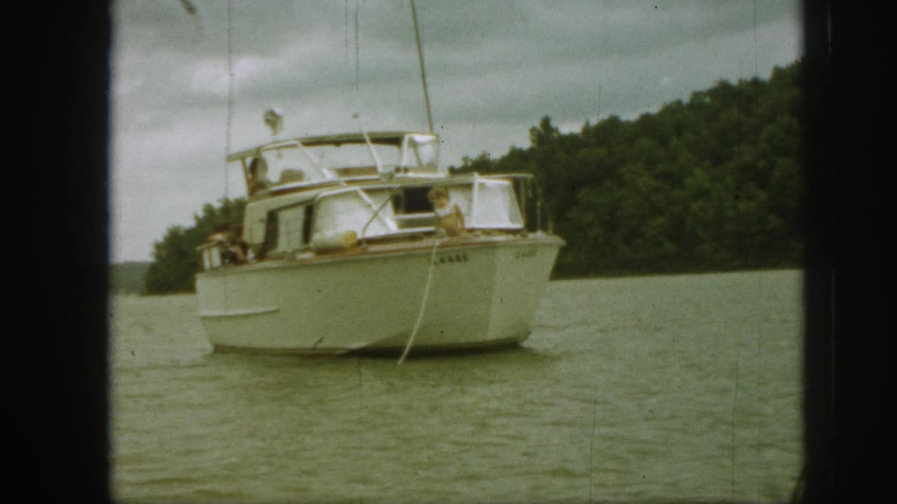 1961 Michigan 8mm frame showing a white motorboat with people aboard on a calm lake near trees.