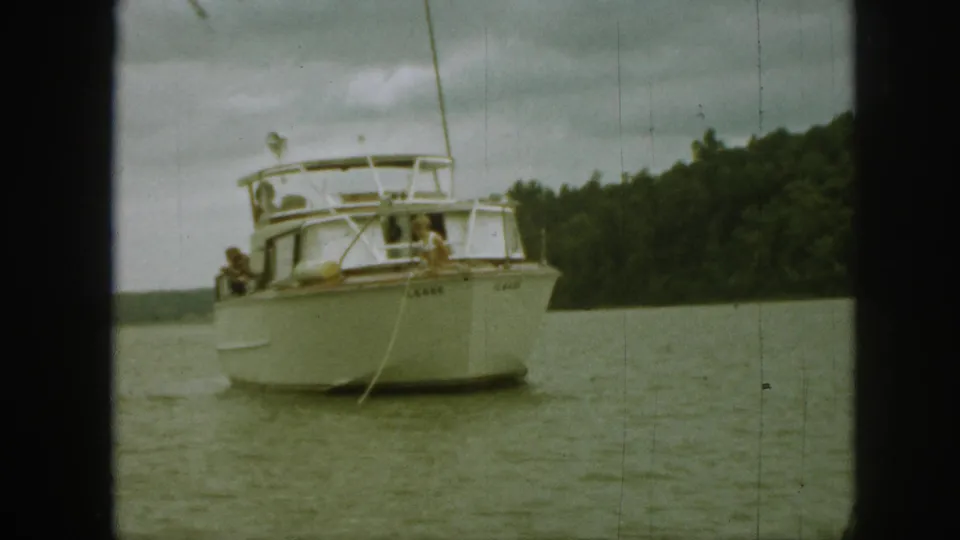 White motorboat on a Michigan lake, with people aboard and a rope or line hanging from the bow.