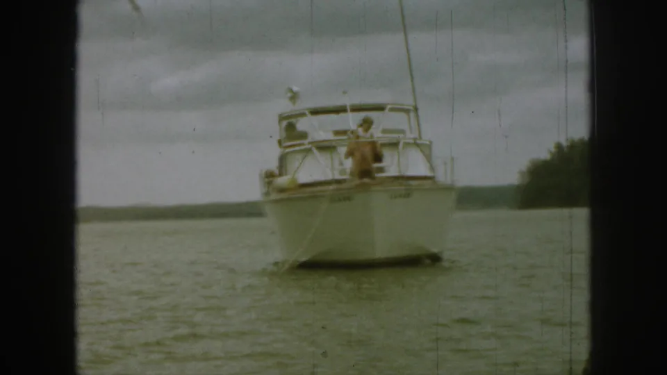 A man on the bow of a white motorboat appears to handle or throw an object while the boat sits on a Michigan lake.