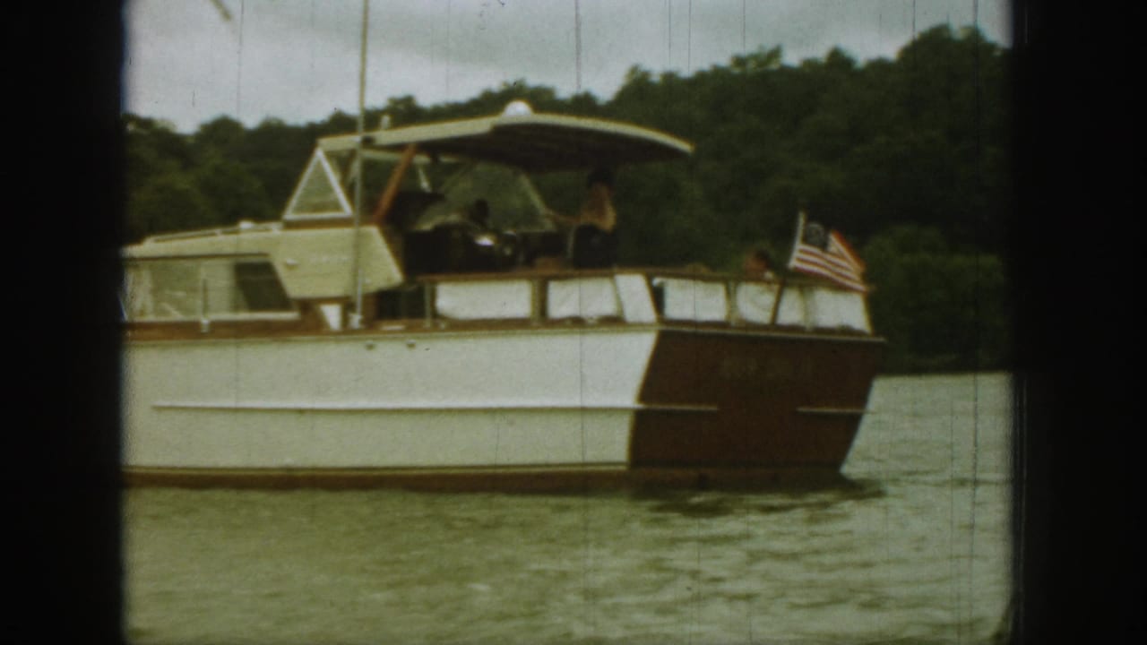 1961 Michigan 8mm frame showing a cabin-style recreational motorboat with occupants and a U.S. flag on a calm lake.