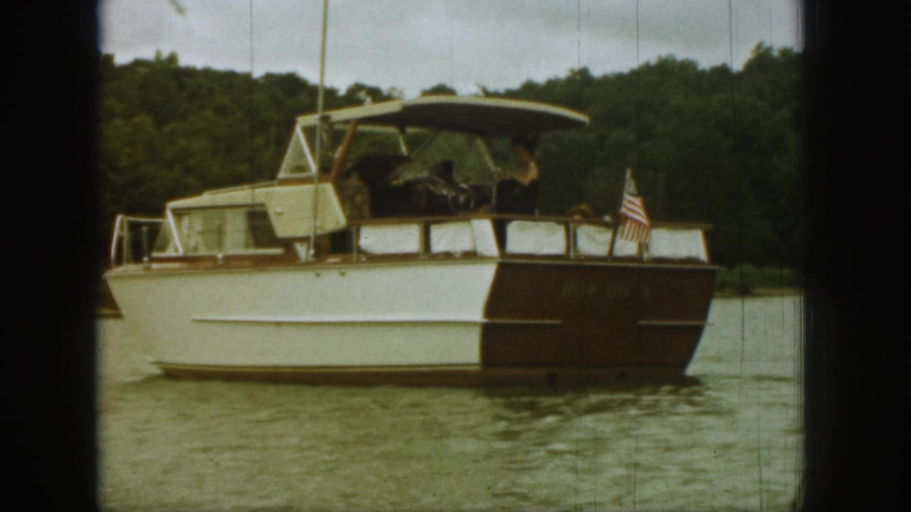 Motorboat seen closer from the side with occupants under the canopy and flag at the stern.