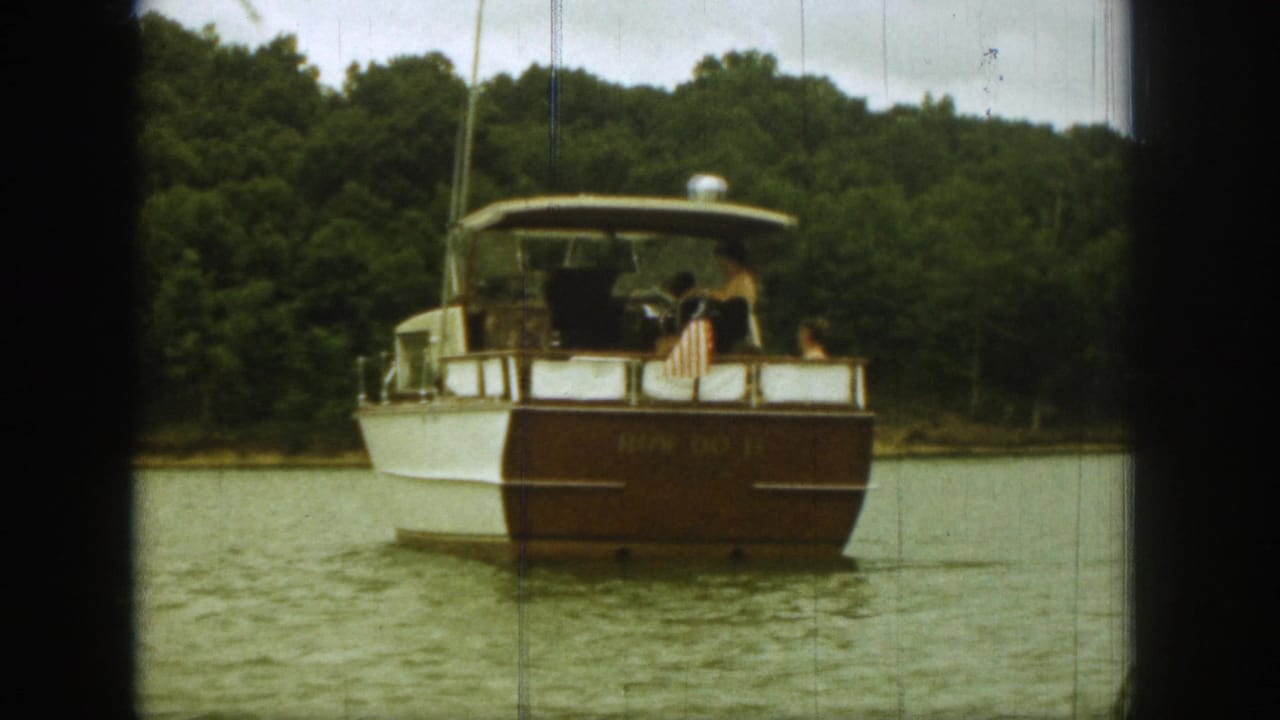 1961 Michigan home-movie frame showing a classic white and brown motorboat from behind on a wooded lake.