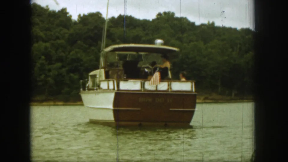 1961 Michigan home-movie frame showing a classic white and brown motorboat from behind on a wooded lake.