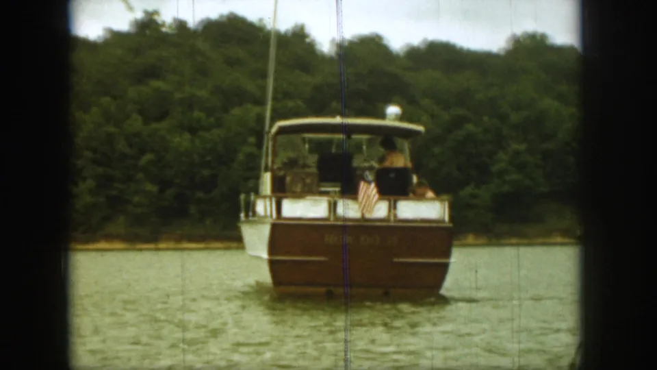 Classic motorboat on a Michigan lake in 1961, with passengers aboard and trees lining the far shore.
