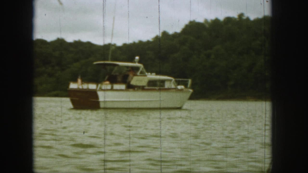 White and brown motorboat on a lake with trees behind it.