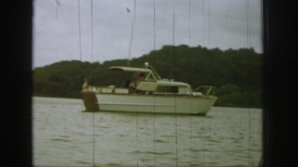 1961 Michigan 8mm frame showing the motorboat broadside, with passengers faintly visible under the canopy and trees beyond.