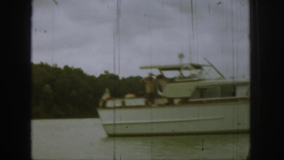 Side view of the white cabin cruiser in Michigan, with visible passengers, calm water, and a dark wooded shoreline.