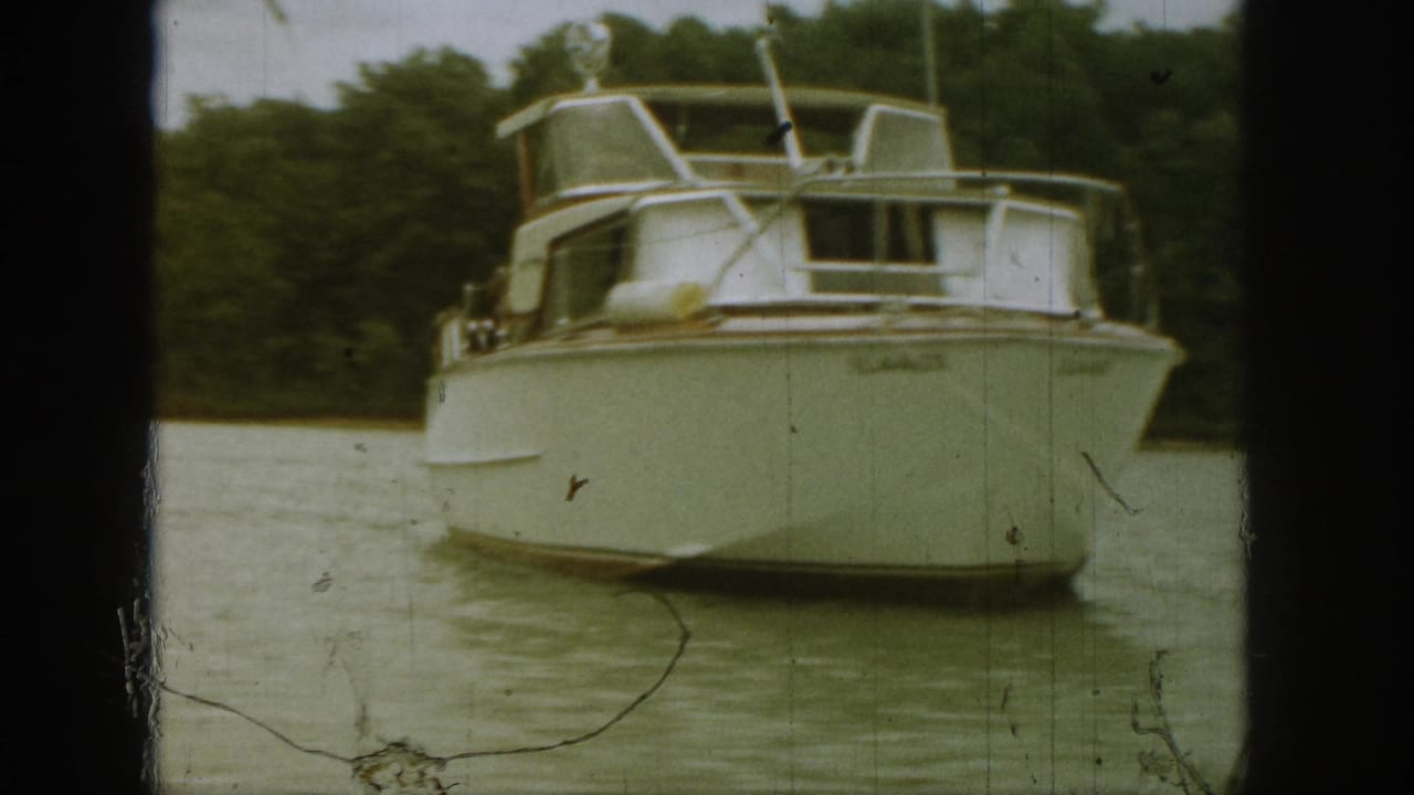 White motorboat facing the camera on a lake with trees behind it.