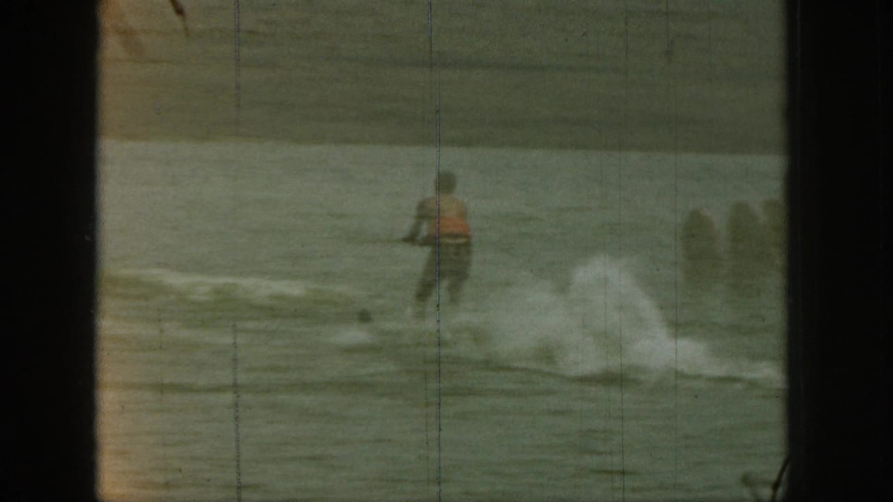 1961 Michigan 8mm frame showing a water skier in a red vest practicing on the lake, with spray rising behind him.