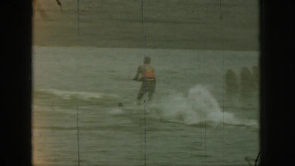 1961 Michigan 8mm frame showing a water skier in a red vest practicing on the lake, with spray rising behind him.