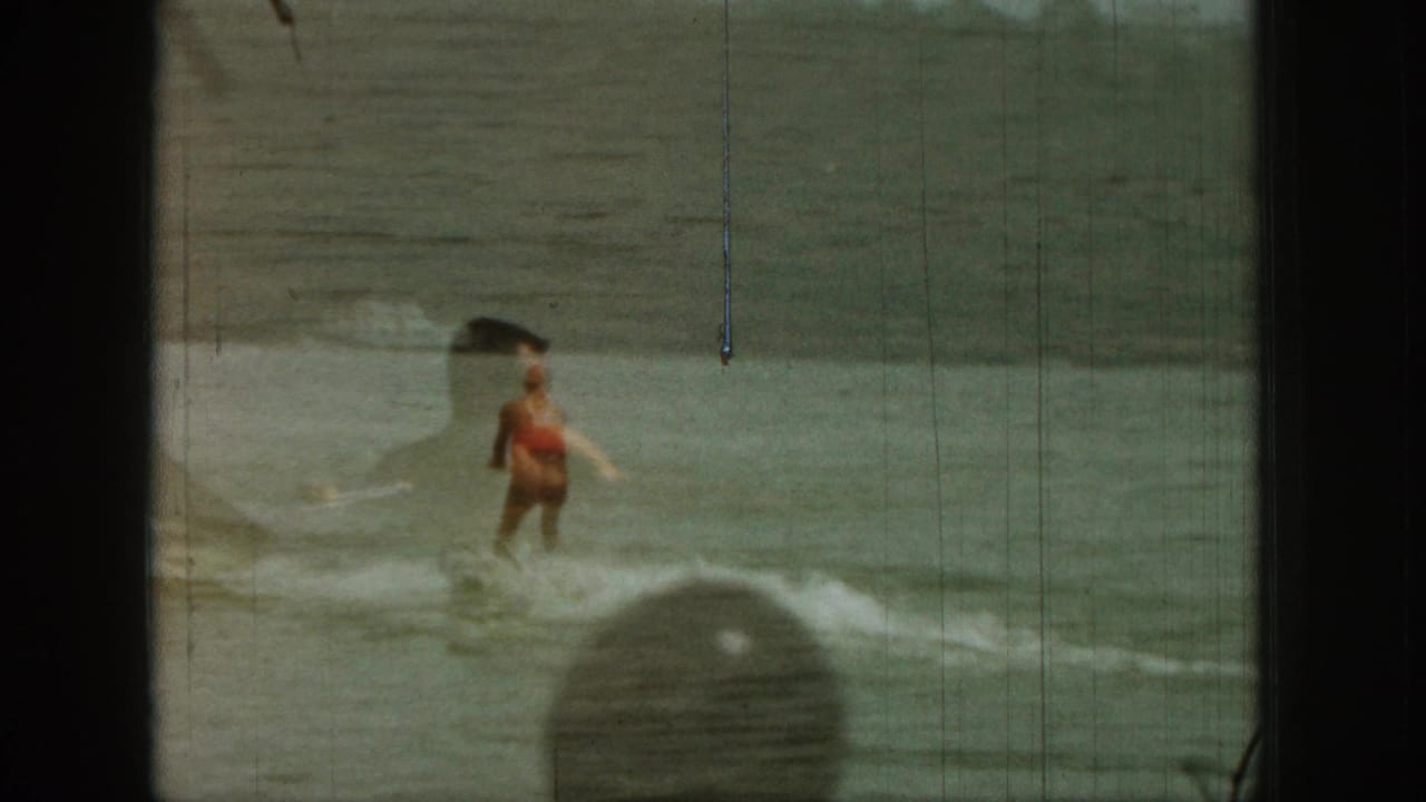 1961 Michigan 8mm frame of a water skier in a red vest crossing the lake, with spray, soft focus, and visible film wear.