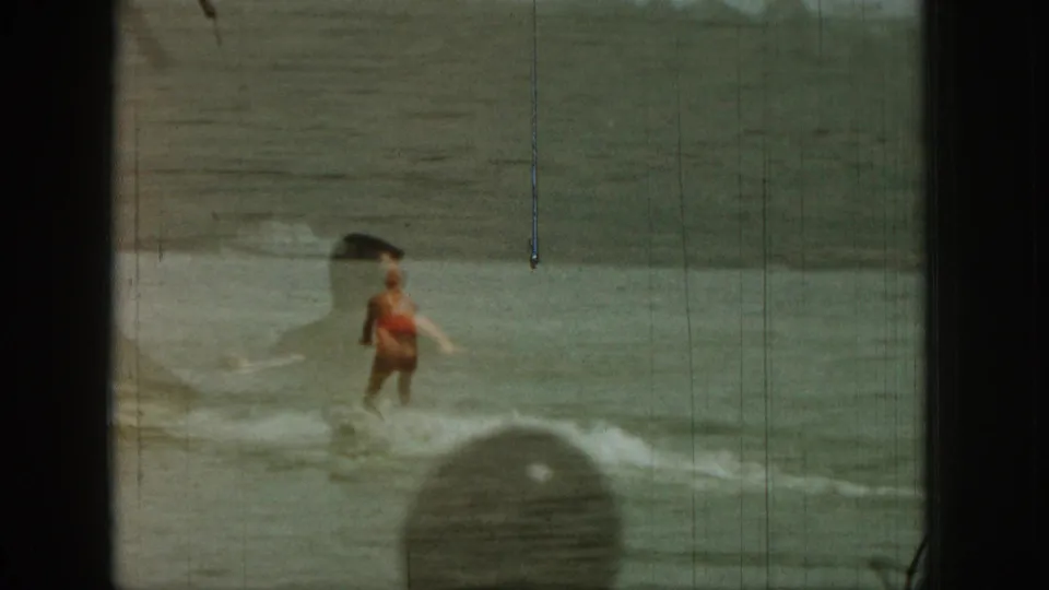 1961 Michigan 8mm frame of a water skier in a red vest crossing the lake, with spray, soft focus, and visible film wear.