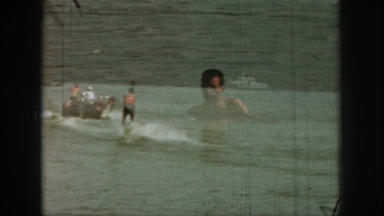 Small boat pulls a waterskier as a man's head and shoulders overlap the right side of the frame.