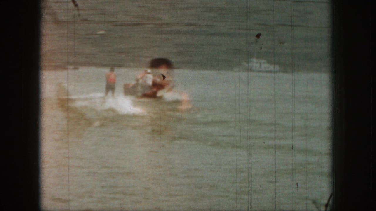 Soft 8mm frame from 1961 Michigan with waterskiing action partly obscured by an overlapping floating figure.