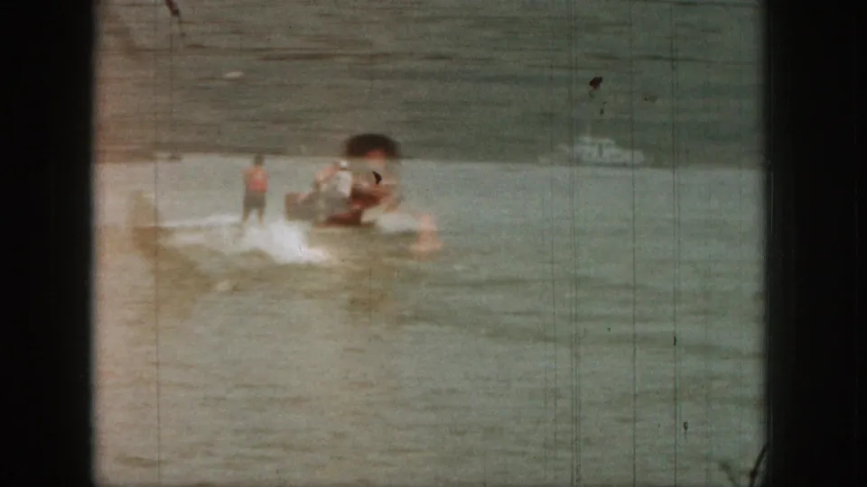 Soft 8mm frame from 1961 Michigan with waterskiing action partly obscured by an overlapping floating figure.