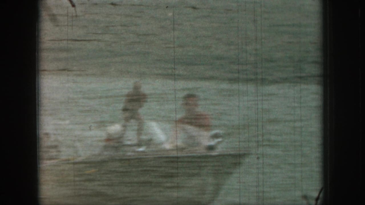 1961 Michigan lake frame with a ghosted man in the water and a blurred watersport figure beside wake or spray.