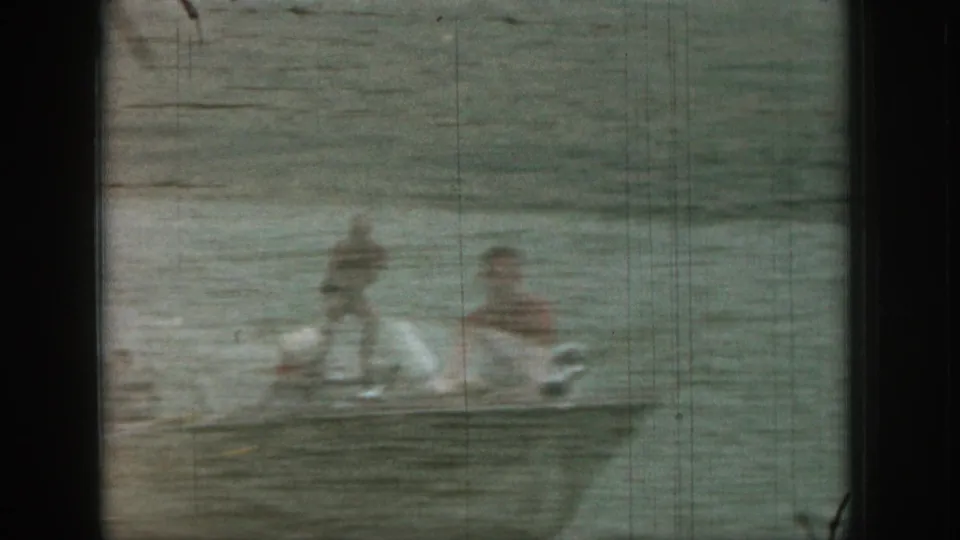 1961 Michigan lake frame with a ghosted man in the water and a blurred watersport figure beside wake or spray.