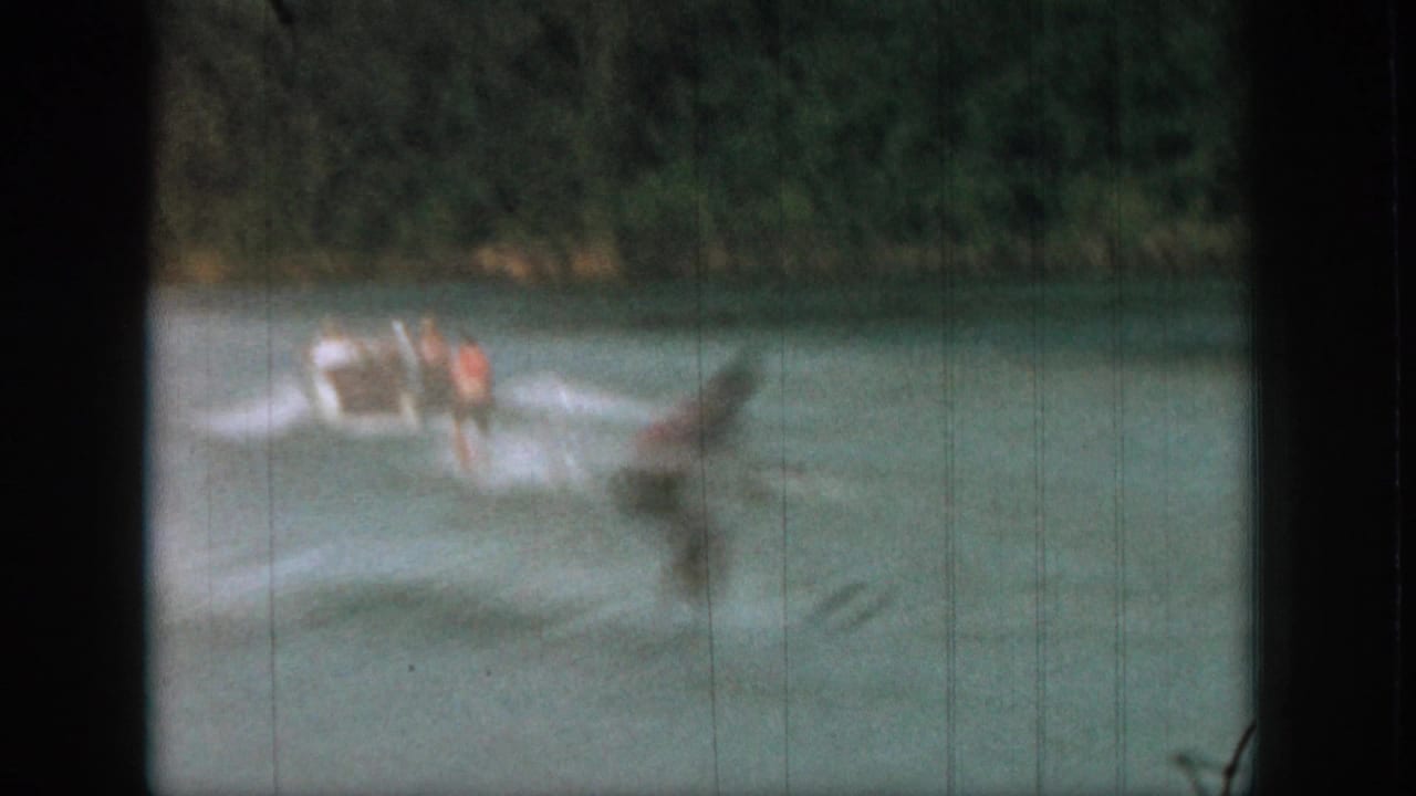 Blurred water skier rides across the river near a small motorboat and foamy wake.
