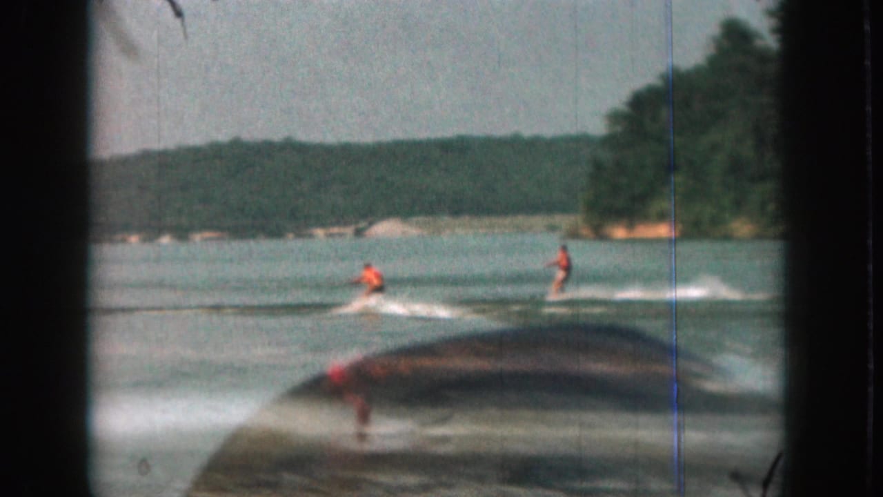 1961 Michigan 8mm frame with two water skiers in orange life vests and a blurred boat shape crossing the foreground.