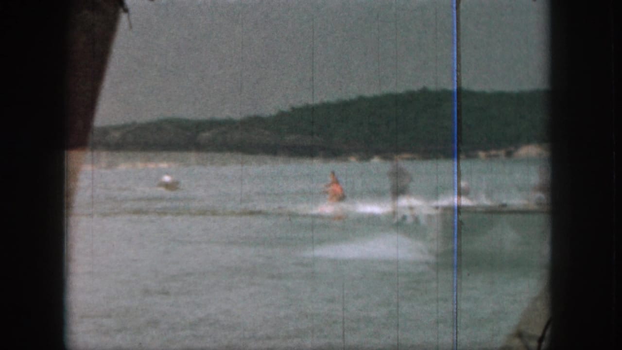 1961 Michigan 8mm frame showing a distant water skier in an orange life vest on open lake water beneath hazy hills.