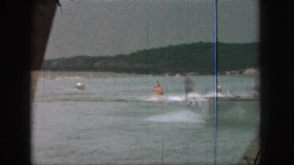 1961 Michigan 8mm frame showing a distant water skier in an orange life vest on open lake water beneath hazy hills.