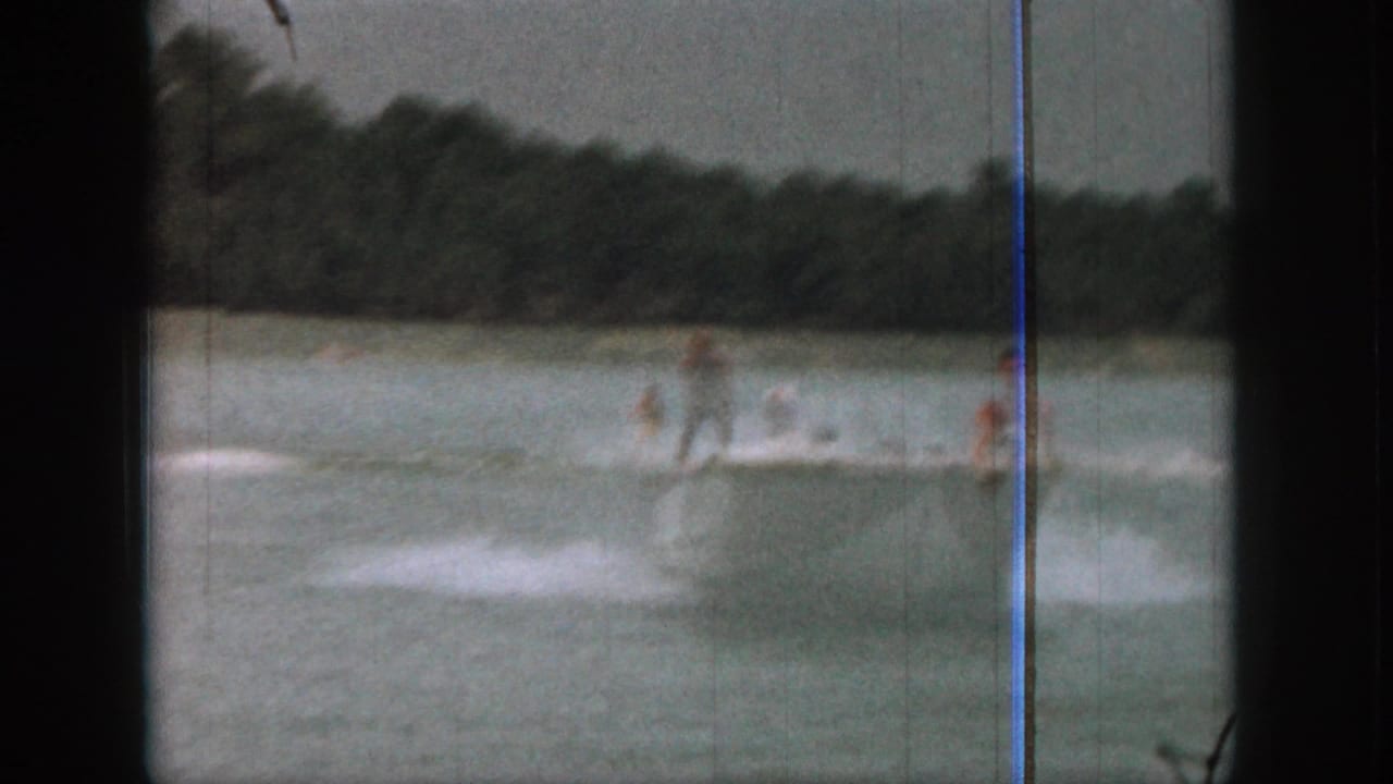Two distant water skiers follow a small motorboat across a calm lake.