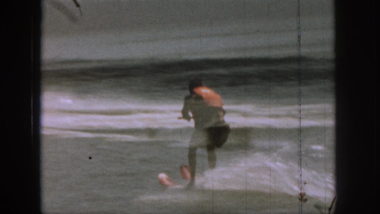 1961 Michigan 8mm frame showing a man water skiing across a lake, with spray behind him and dark film-frame edges visible.