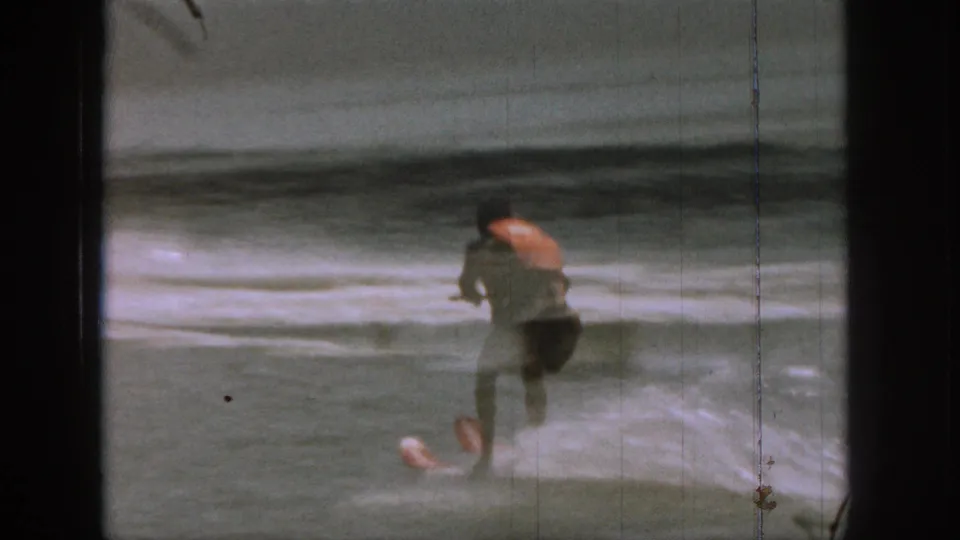 1961 Michigan 8mm frame showing a man water skiing across a lake, with spray behind him and dark film-frame edges visible.